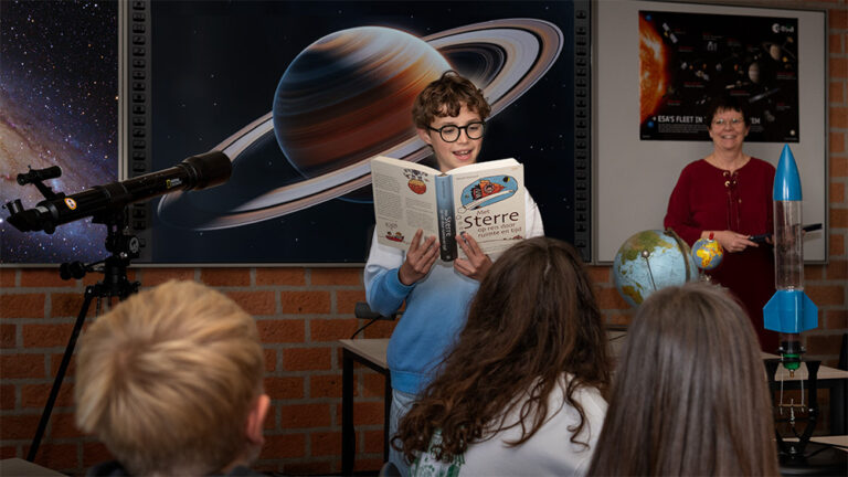 leerling met bril leest voor uit een boek over de sterren